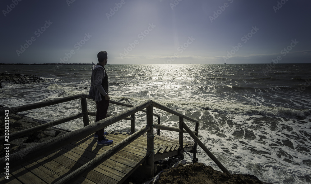 Hombre joven de pie en el muelle mirando al mar