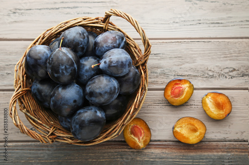 Fotografía Ripe and sweet plums in basket on wooden table