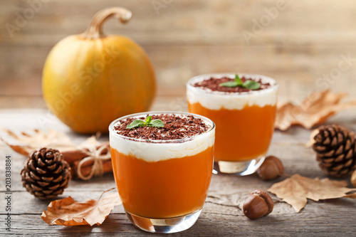 Pumpkin smoothie in glasses with dry leafs and acorns on wooden table