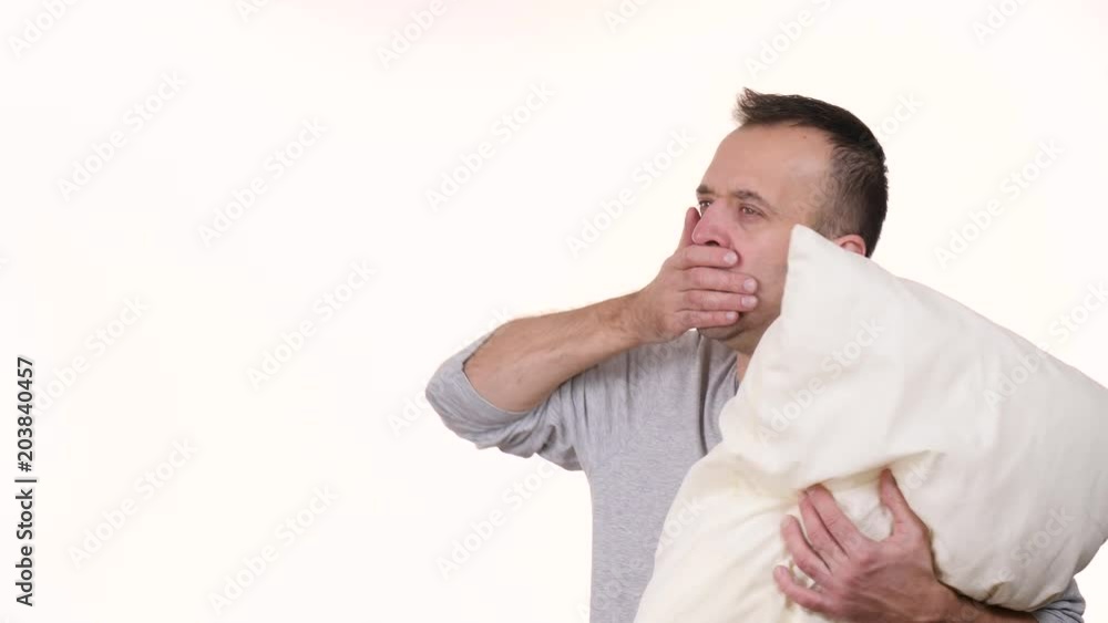 Man sleepy tired wearing nightwear holding pillow yawning. Health balance sleep deprivation concept. Male at morning with lack of slumber, on white. Slow motion. Man sleepy tired wearing nightwear holding pillow yawning. Health balance sleep deprivation concept. Male at morning with lack of slumber, on white. Slow motion.