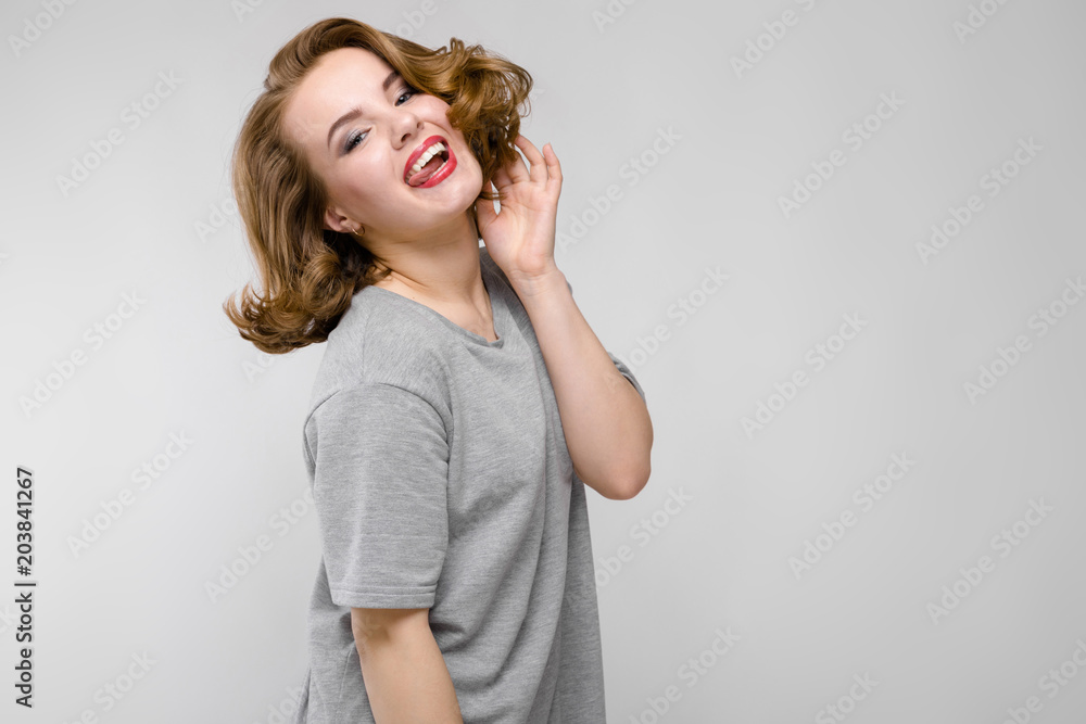Charming young girl in a gray T-shirt on a gray background. The girl bowed her head to her side and stuck out her tongue Charming young girl in a gray T-shirt on a gray background. The girl bowed her head to her side and stuck out her tongue