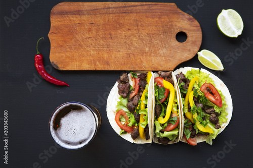 Tacos with beef and vegetables, beer and lime on a black background, top view. Mexican kitchen. Copy space. photo