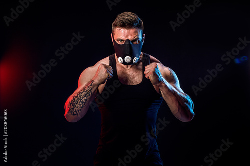 Strong male athlete in a black training mask posing on a black background photo