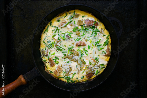 Scrambled eggs with herbs, bread, meat, onions and garlic in a frying pan on a dark background. Low key. Selective focus. Top view