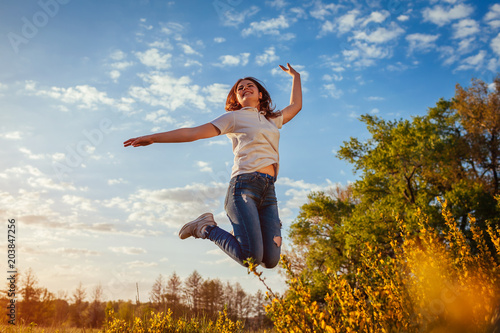 Young woman jumping and having fun in spring field at sunset. Happy and free girl enjoys nature