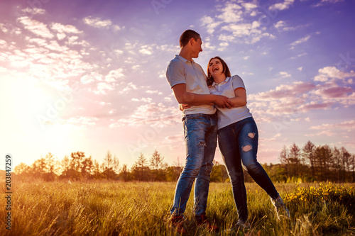 Couple having fun in spring field. Young man and girl hugging and laughing at sunset.