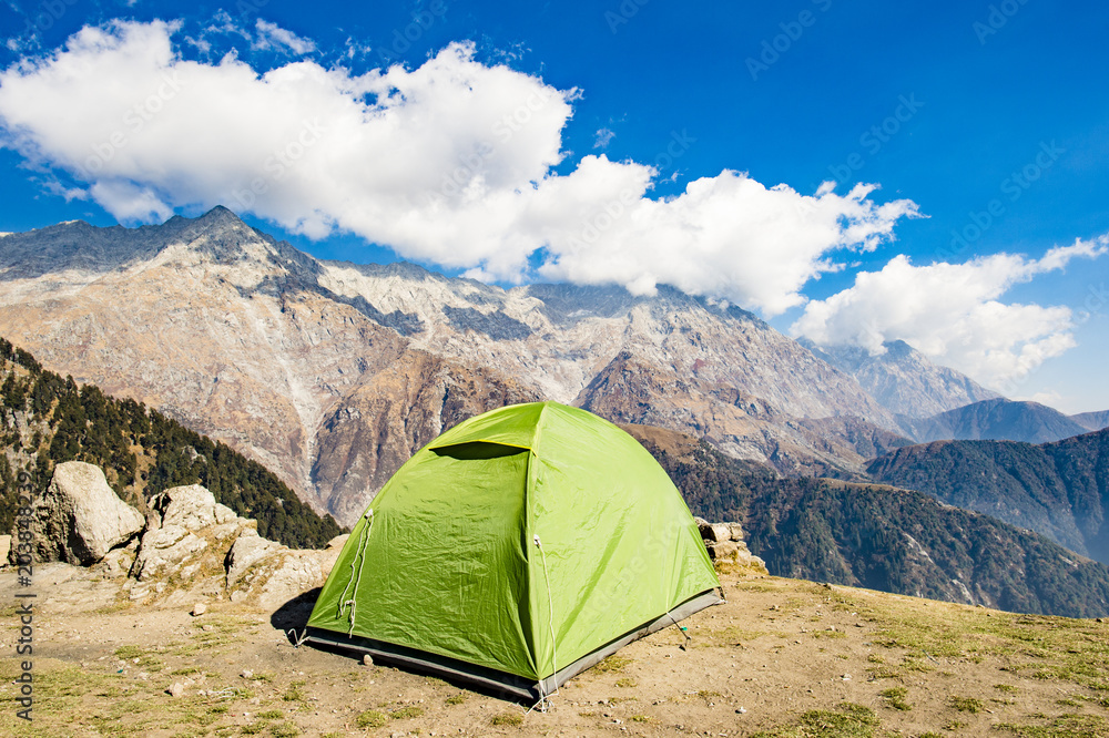 A single green tent seen against Dhaulahaar peaks of Himalayas in Triund. Sunny day whit some clouds. Dharamshala, Himachal Pradesh. India