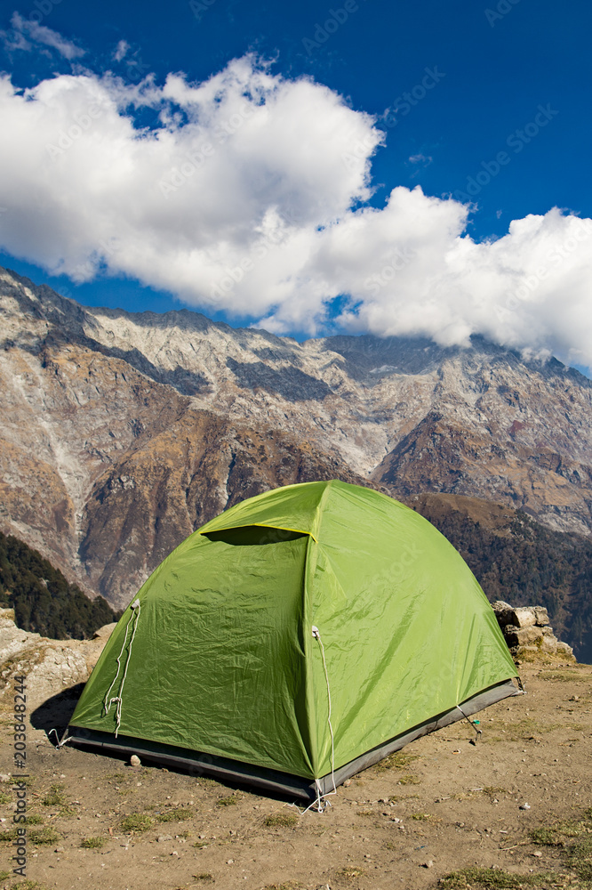 A single green tent seen against Dhaulahaar peaks of Himalayas in Triund. Sunny day whit some clouds. Dharamshala, Himachal Pradesh. India