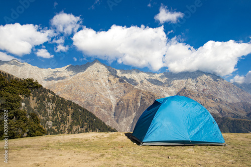 A single blue tent seen against Dhaulahaar peaks of Himalayas in Triund. Sunny day whit some clouds. Dharamshala  Himachal Pradesh. India