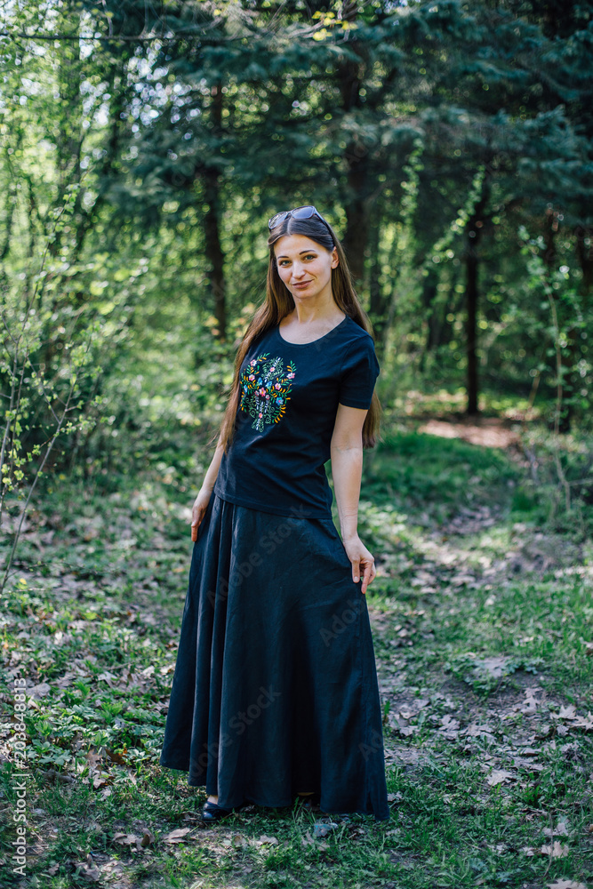 Girl in long black dress with embroidery walks through the woods