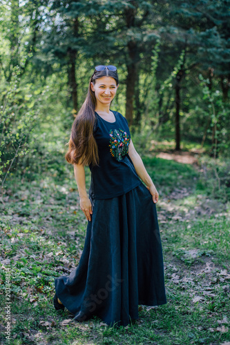 Smiling girl in long black dress with embroidery walks through the woods