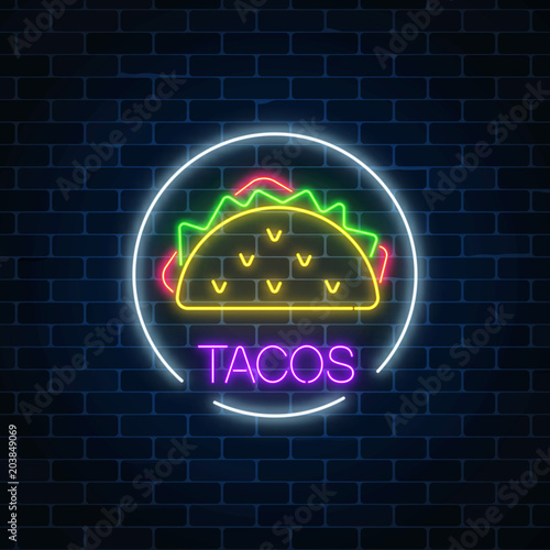 Neon glowing sign of tacos in circle frame on a dark brick wall background. Fastfood light billboard symbol.