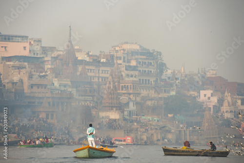 Obraz na płótnie A man is sailing on his wooden boat in the sacred river Ganges in the city of Varanasi at sunset. Blurred Manikarnika ghat on background. w salonie
