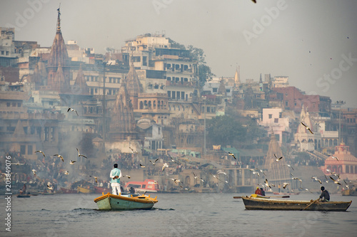 Obraz na płótnie A man is sailing on his wooden boat in the sacred river Ganges in the city of Varanasi at sunset. Blurred Manikarnika ghat on background. w salonie