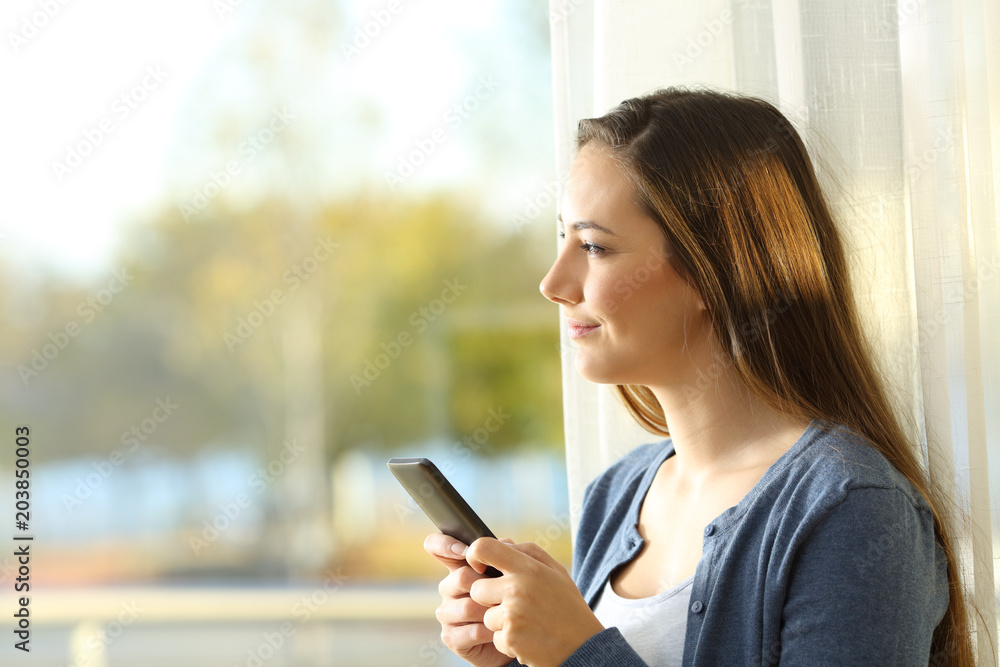 Woman using a smart phone looking outdoors at home