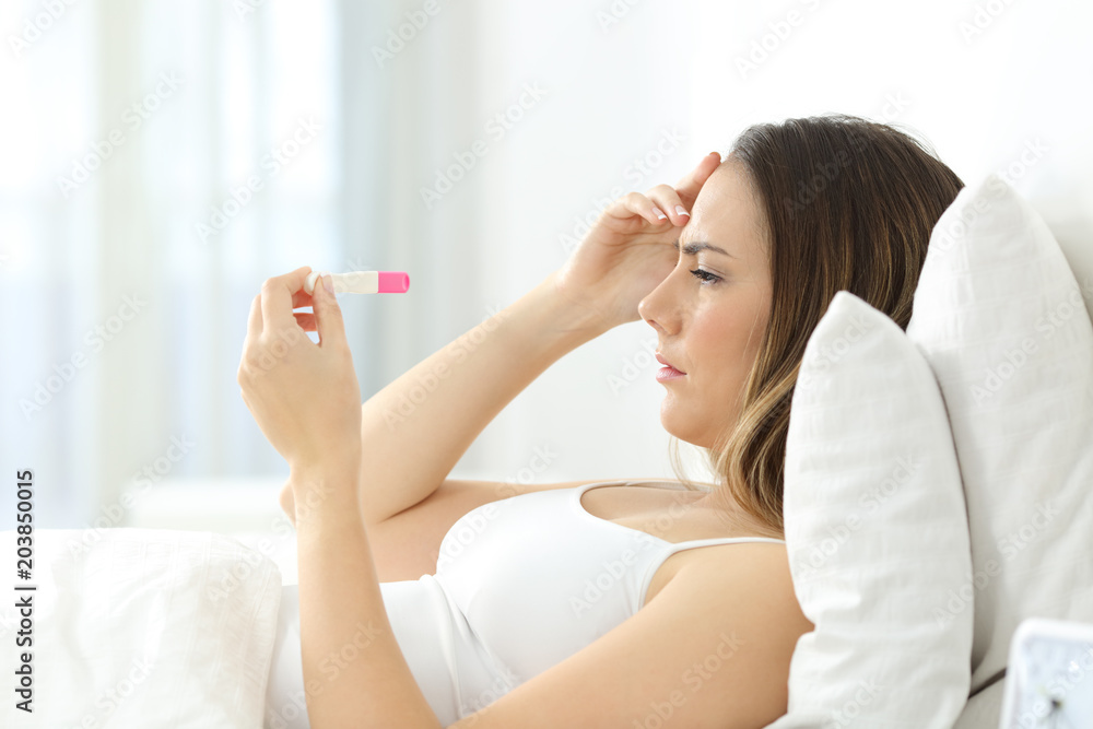 Worried woman checking a pregnancy test on the bed Worried woman checking a pregnancy test on the bed