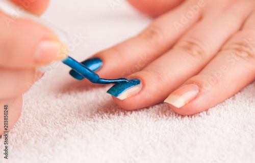 Woman applying dark blue shiny nail polish on middle finger