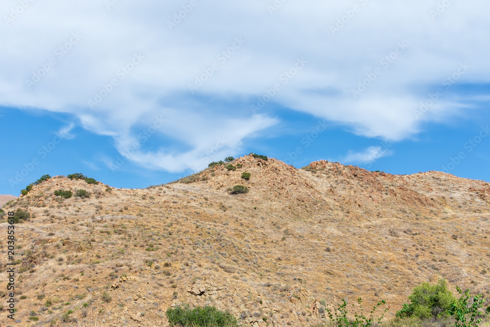 Blue sky and white clouds over extremely dry hillside in desert