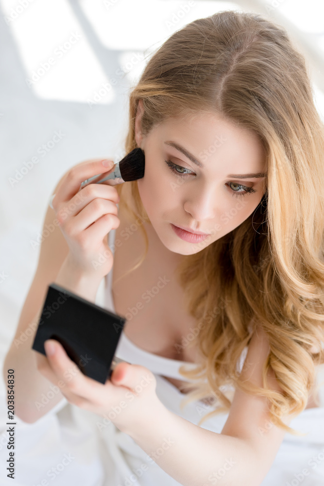 attractive girl applying blush with brush and looking at mirror attractive girl applying blush with brush and looking at mirror