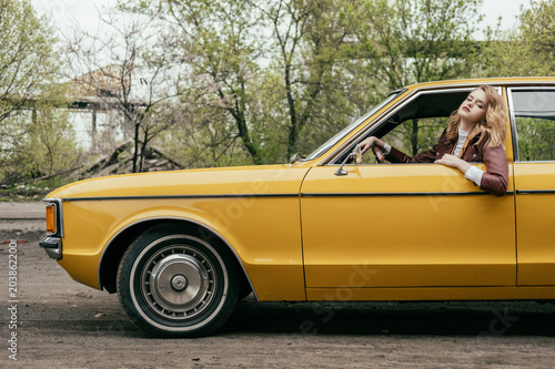 side view of beautiful young woman looking at camera while sitting in yellow classic car © LIGHTFIELD STUDIOS