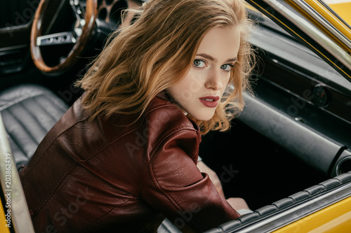 high angle view of beautiful young woman sitting in retro car and looking at camera