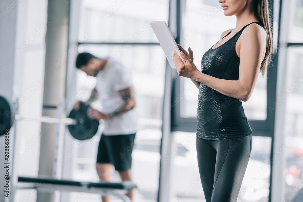 cropped image of female personal trainer with digital tablet and athletic man with barbell at gym cropped image of female personal trainer with digital tablet and athletic man with barbell at gym