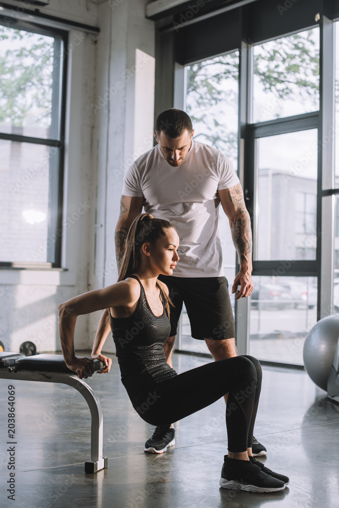 male personal trainer looking at sportswoman doing plank at gym male personal trainer looking at sportswoman doing plank at gym