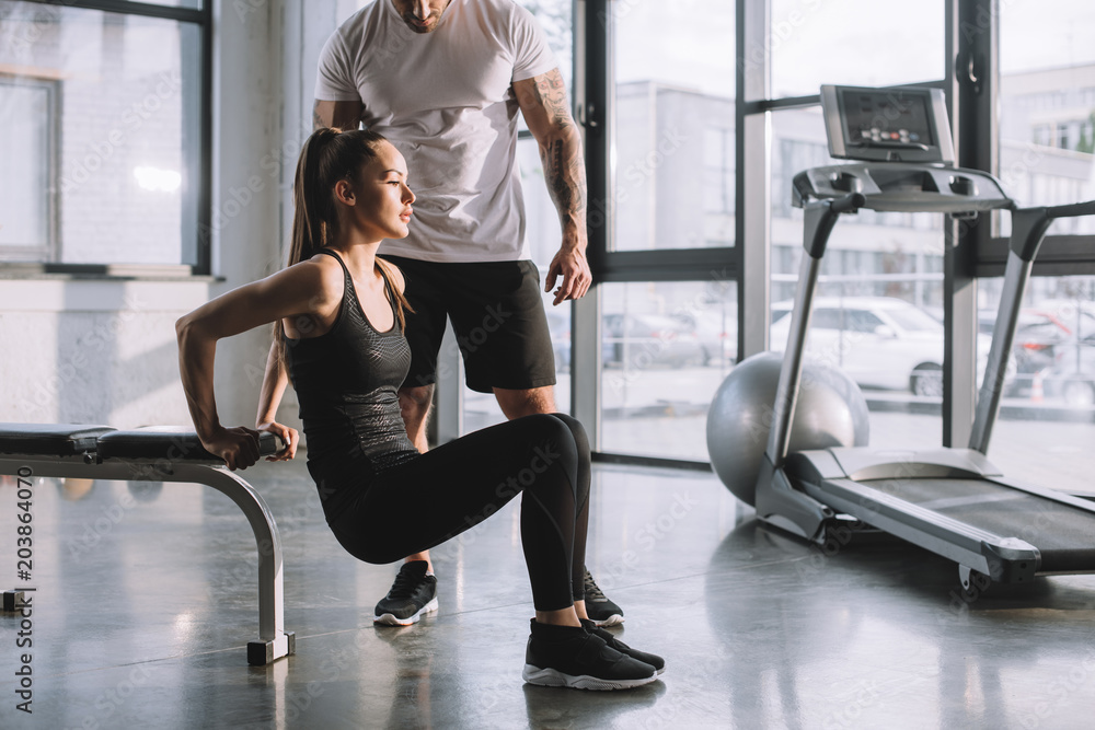 Fototapeta premium male personal trainer looking at sportswoman doing plank at gym
