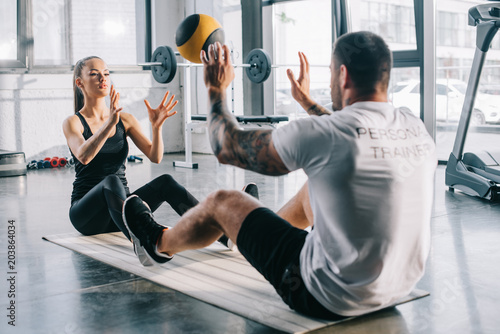 male personal trainer and sportswoman doing exercises with ball at gym