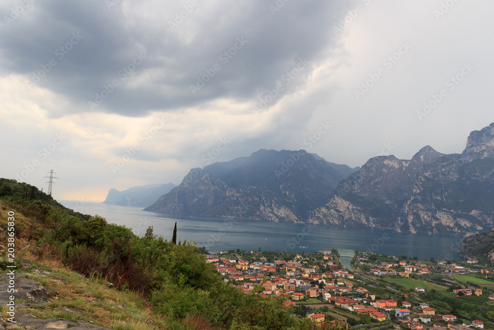 Panorama of Lake Garda, lakeside village Torbole and mountains with dark storm clouds, Italy