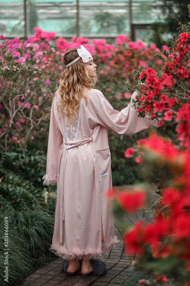 Beautiful sexy girl wearing pink bathrobe and lingerie standing in flower  garden. Vertical full lenght portrait Stock Photo