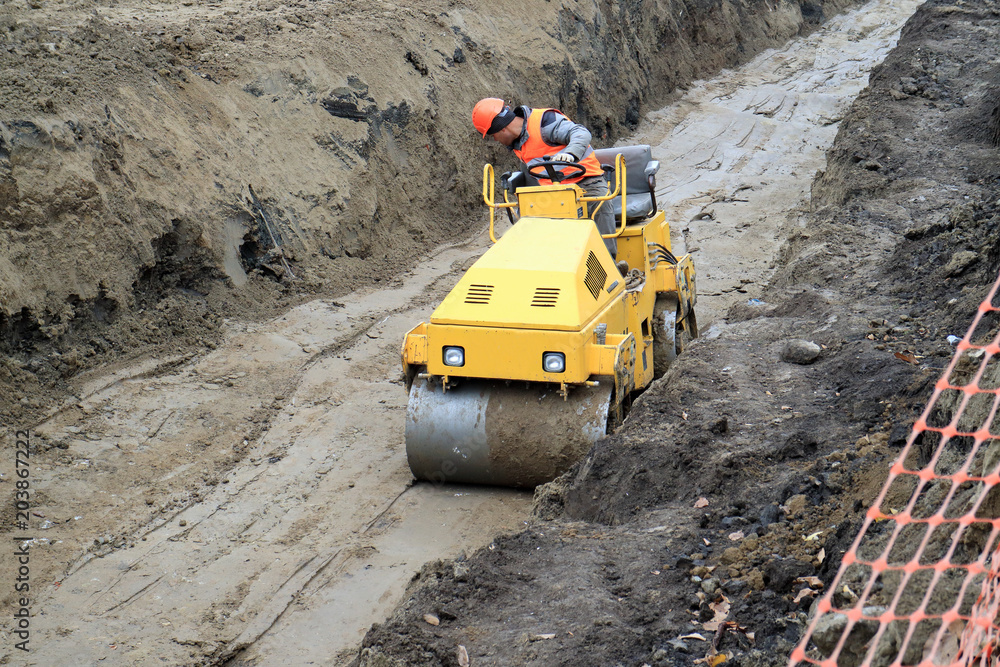road roller compacts the sand in a deep trench. road roller compacts the sand in a deep trench.