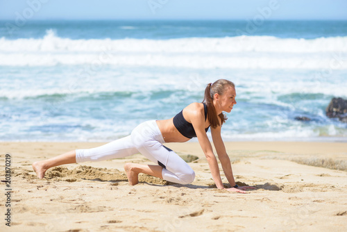 Smiling active young woman doing sports excercises on the beach