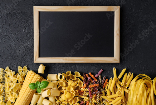 Raw Italian pasta fettuccine, paccheri, farfalle, spaghetti, fusilli, penne, conchiglie on a dark background.