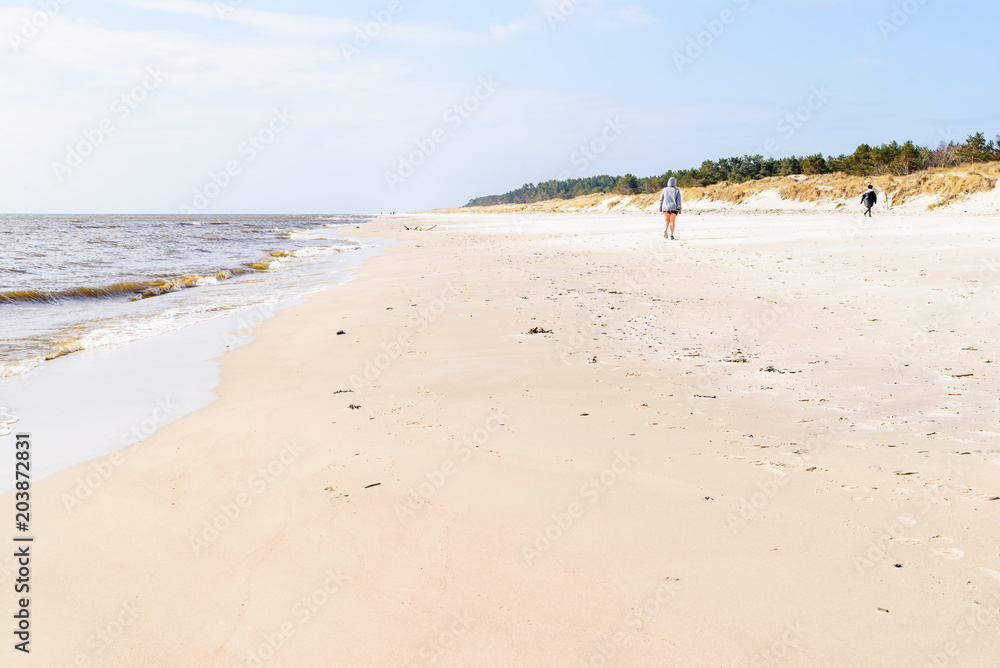 Spraggehusen, Sweden - Two persons walking away on the sandy beach on a sunny spring day.