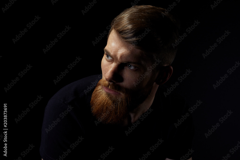 Image of single standing in profile young handsome serious bearded man over black background with copy space. Image of single standing in profile young handsome serious bearded man over black background with copy space.