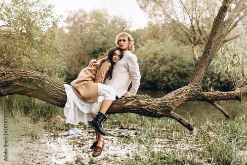 A beautiful couple in the boo style embraces sitting on a branch over the lake photo