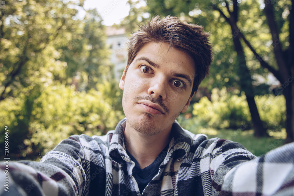 handsome young man looking at the camera and taking a selfie photo outdoors. handsome young man looking at the camera and taking a selfie photo outdoors.