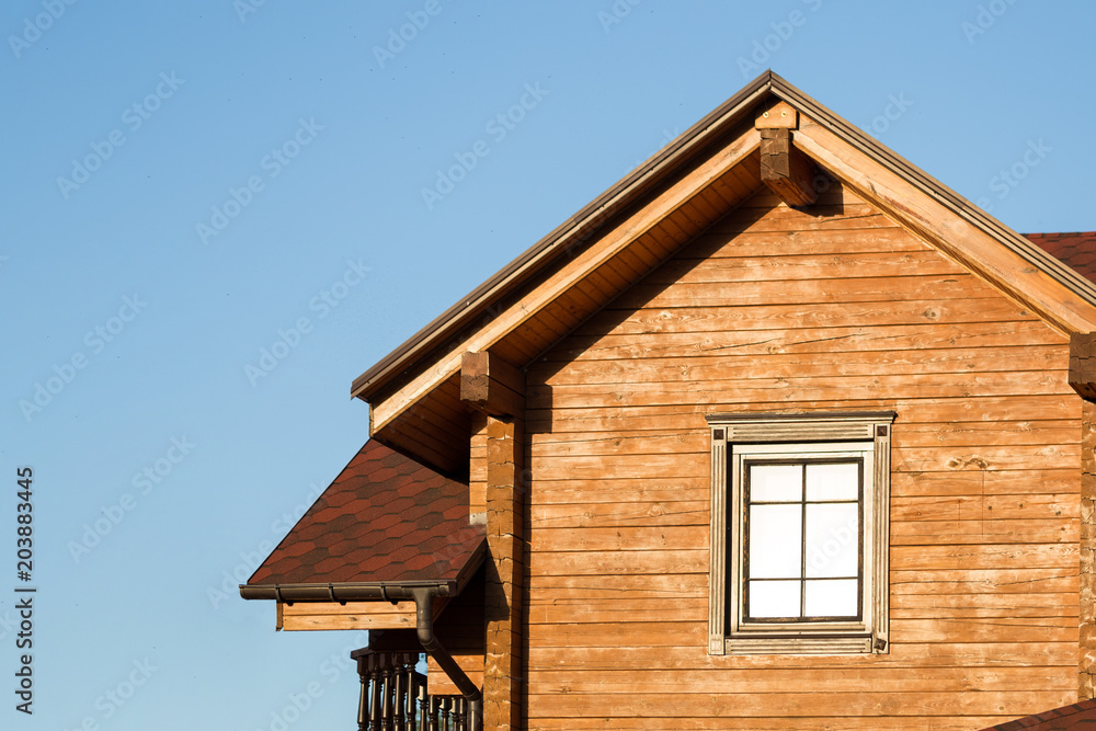 Part of modern wooden country house with blue sky on background. Roof of eco residential building near forest. Building and architecture of rustic chalet