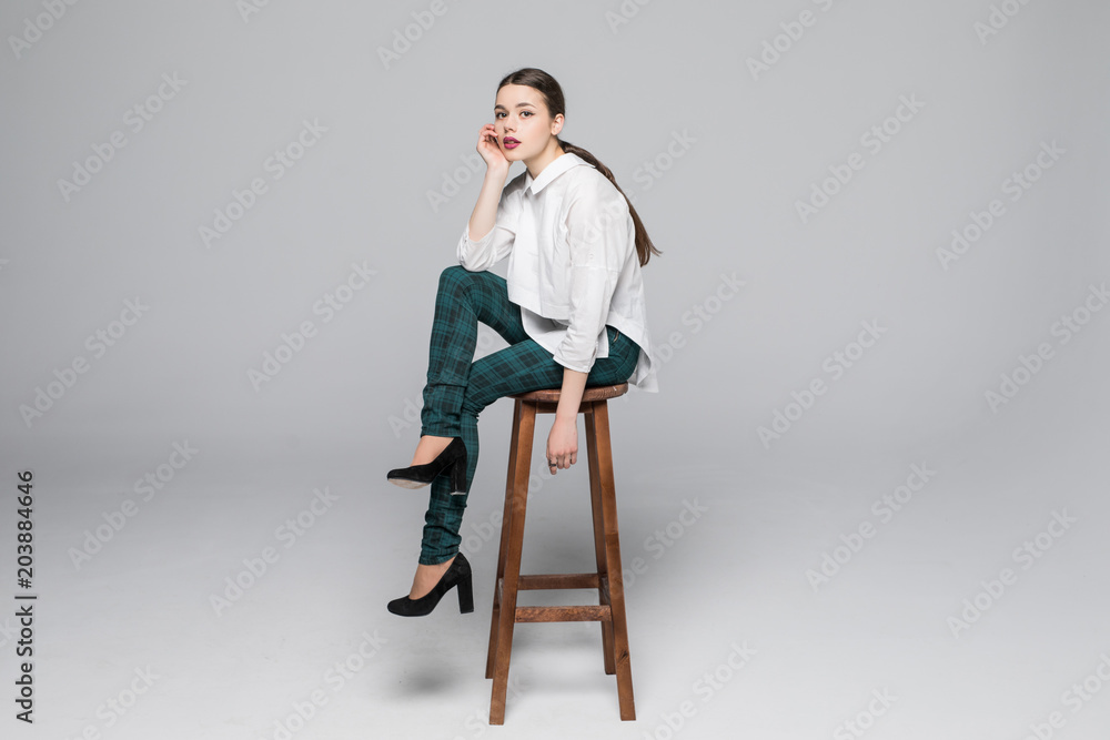 Full length portrait of a young woman sitting on chair over gray background Full length portrait of a young woman sitting on chair over gray background