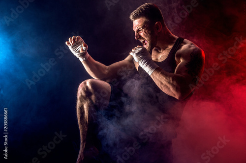 Sport concept. Sportsman muay thai boxer fighting on black background with smoke. Copy Space. photo