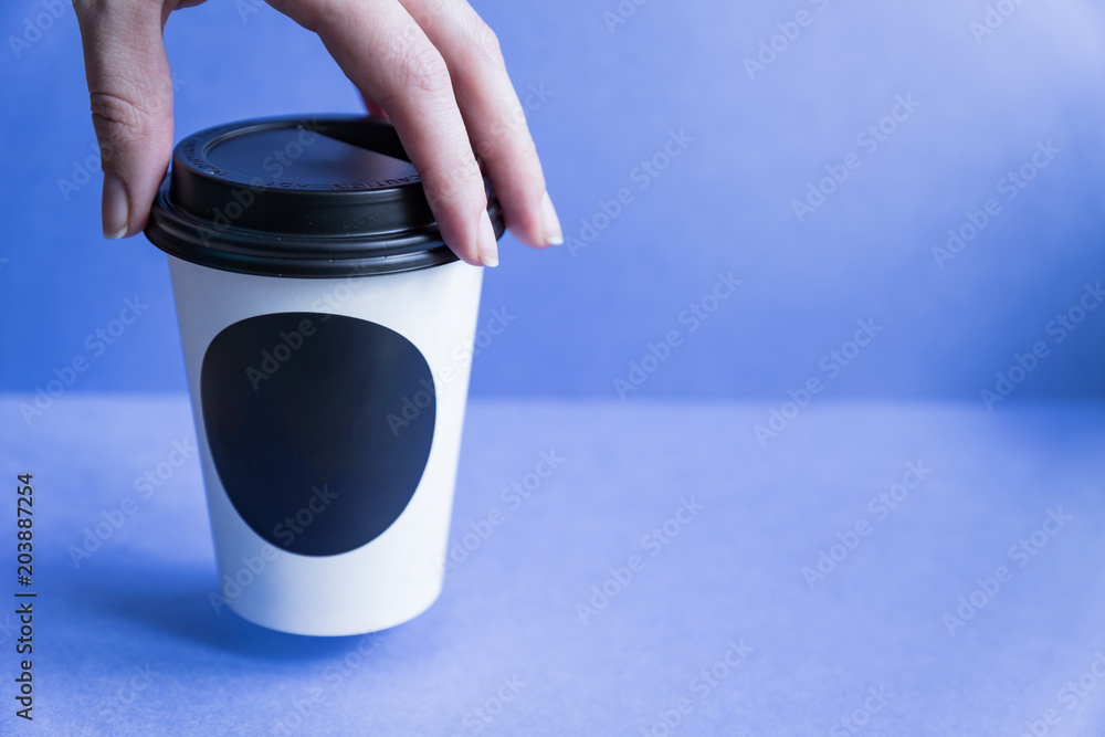 white paper kraft disposable cup for coffee with black plastic lid in a female hand. coffe to go on blue background. white paper kraft disposable cup for coffee with black plastic lid in a female hand. coffe to go on blue background.
