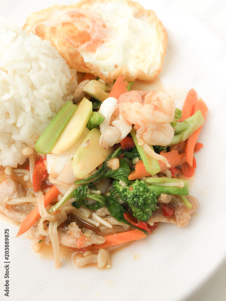 Fried Savory sauteed mixed vegetables with shimp and fried egg served with rice in white dish on white background as Thai homemade meal or recipe in the restaurant. Thai style food. Fried Savory sauteed mixed vegetables with shimp and fried egg served with rice in white dish on white background as Thai homemade meal or recipe in the restaurant. Thai style food.