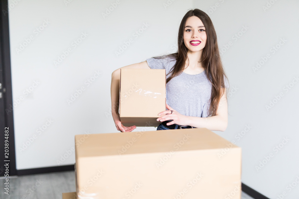 Young woman lifting cardboard box while moving home, smiling. Young woman lifting cardboard box while moving home, smiling.