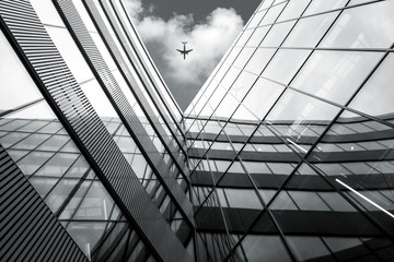 Flying airplane over modern architecture building, low angle black and white high contrast picture 