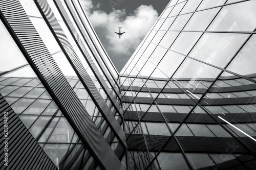 Flying airplane over modern architecture building, low angle black and white high contrast picture 