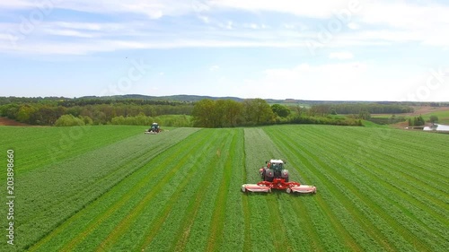 Aerial view of two modern tractors mowing a green fresh grass field on a sunny day with blue sky. 