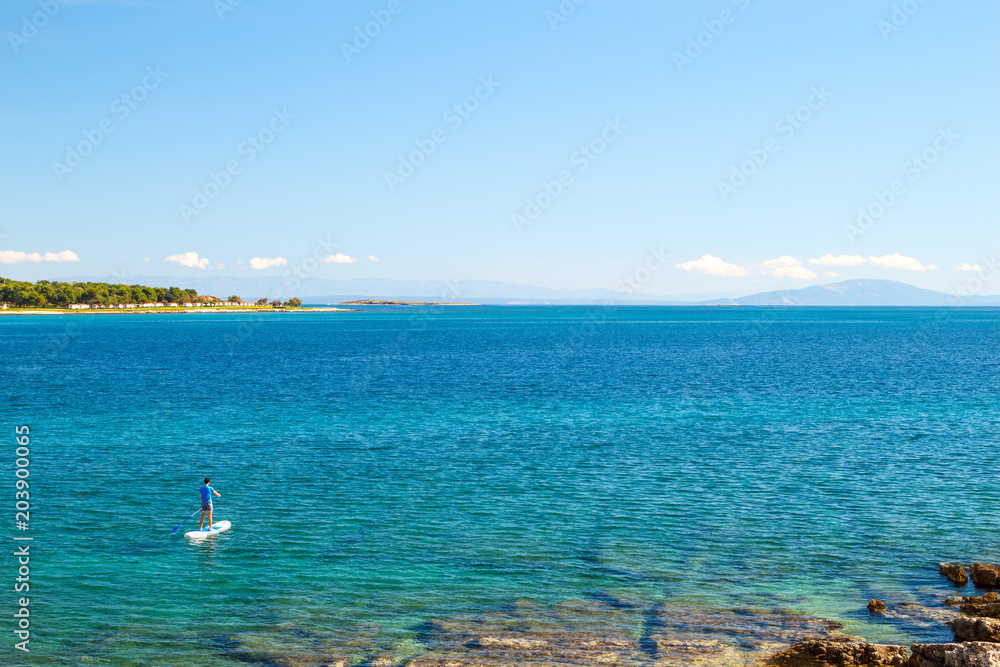 Man on SUP. Stand Up Paddling. Blue Sea Water. Floating Sup Board. Summer Vacation and Outdoor Sport Concept. Panoramic Photo with Copy Space.