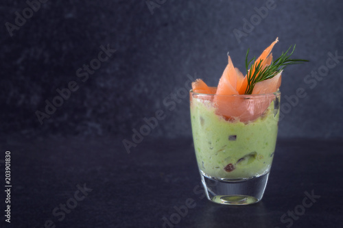 party appetizer, avocado cream with salmon and dill garnish in a glass on a dark slate background with copy space