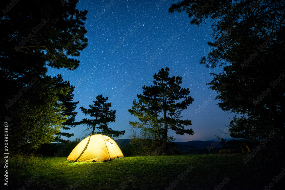 Glowing camping tent in the night mountain forest under a starry sky ...
